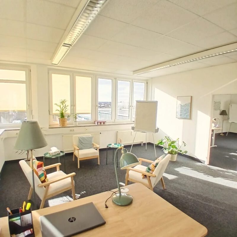 Raum von Care Together mit drei Stoffsesseln, Schreibtisch, Flipchart und Blick aus dem Fenster.